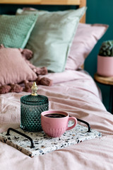 Fototapeta na wymiar Stylish composition of bedroom interior with lastrico tray with coffee and elegant personal accessories. Beautiful pink and green bed sheets, blanket and pillow. Template Design home staging. Close up