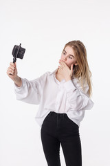 happy girl makes self portrait with smartphone attached to small tripod. young pretty blond female with long hair sending air kiss, using cell phone isolated on white background. teen communication