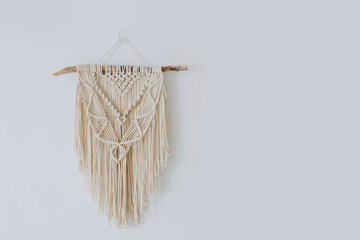 Handmade stylish cotton macrame decoration hanging on a white empty wall. Copy space.