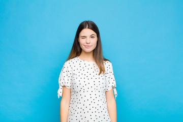 young pretty woman looking happy and friendly, smiling and winking an eye at you with a positive...