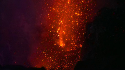 Fototapeta na wymiar CLOSE UP: Stunning shot of a volcano erupting and spewing out hot lava at night.