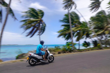Young man speeds past the palm trees and exotic beaches on his motorcycle.
