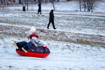 Fototapeta na wymiar Child having fun on snow tube in a park, boy sliding down the hill. Winter entertainment, sledding in frosty day