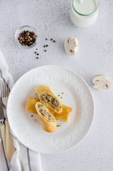 Traditional Russian thin pancakes or crepes stuffed with mushrooms with onion, garlic, herbs, cheese and cream on a white plate with sour cream. top view, copy space, horizontal