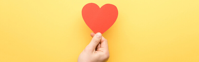 panoramic shot of man holding heart-shaped card isolated on yellow © LIGHTFIELD STUDIOS