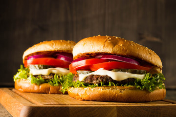 Home made hamburger with beef, onion, tomato, lettuce and cheese. Fresh burger close up on wooden rustic table with potato fries, beer and chips. Cheeseburger.