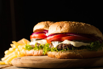 Home made hamburger with beef, onion, tomato, lettuce and cheese. Fresh burger close up on wooden rustic table with potato fries, beer and chips. Cheeseburger.