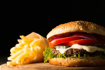 Home made hamburger with beef, onion, tomato, lettuce and cheese. Fresh burger close up on wooden rustic table with potato fries, beer and chips. Cheeseburger.