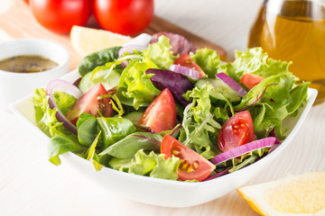 Fresh healthy salad with delicious ruccola, spinach, cabbage, arugula, feta cheese, red onion, cucumber, sesame seeds and cherry tomato on wooden background. Healthy and diet food concept.