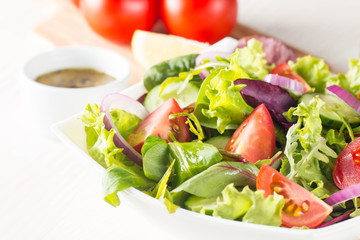 Fresh healthy salad with delicious ruccola, spinach, cabbage, arugula, feta cheese, red onion, cucumber, sesame seeds and cherry tomato on wooden background. Healthy and diet food concept.