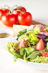 Fresh healthy salad with delicious ruccola, spinach, cabbage, arugula, feta cheese, red onion, cucumber, sesame seeds and cherry tomato on wooden background. Healthy and diet food concept.