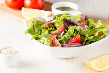 Fresh healthy salad with delicious ruccola, spinach, cabbage, arugula, feta cheese, red onion, cucumber, sesame seeds and cherry tomato on wooden background. Healthy and diet food concept.