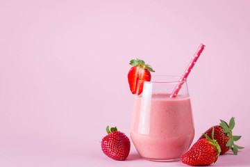 Glass of fresh strawberry milkshake, smoothie and fresh strawberries on pink, white and wooden background. Healthy food and drink concept.