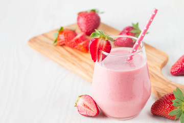 Glass of fresh strawberry milkshake, smoothie and fresh strawberries on pink, white and wooden background. Healthy food and drink concept.