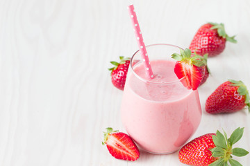 Glass of fresh strawberry milkshake, smoothie and fresh strawberries on pink, white and wooden background. Healthy food and drink concept.