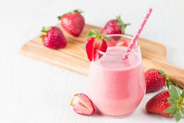 Glass of fresh strawberry milkshake, smoothie and fresh strawberries on pink, white and wooden background. Healthy food and drink concept.