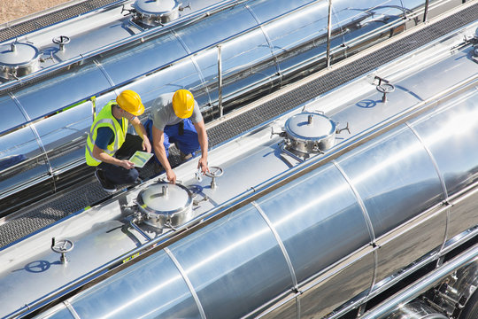 Workers on platform above stainless steel milk tanker