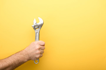 cropped view of man holding spanner on yellow background