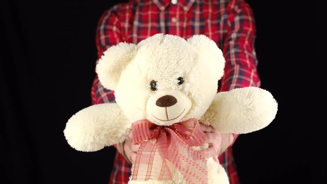 Young man gives a gift soft toy bear on black background. Congratulate Happy New Year, Merry Christmas, Happy Valentine's Day, presents gifts