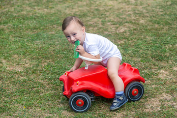 Little boy holding comb while sitting on red color toy car