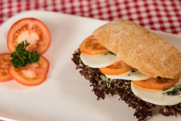 on a white plate lies a sliced bread roll filled with sausage, cheese and egg and as decoration a bunch of radishes