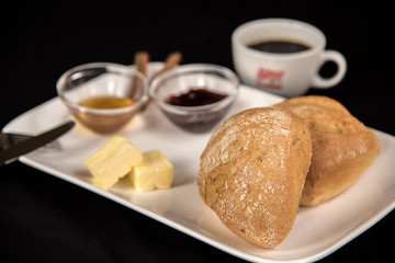 on a dark background stands a plate with a sweet breakfast and a cup of black coffee