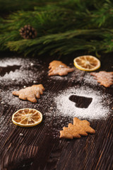 Gingerbread cookies in Christmas fir-tree and heart shape, powdered sugar on wooden background, citrus dried fruits, fir tree branch, angle view, selective focus