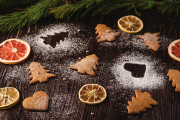 Obraz na płótnie Canvas Gingerbread cookies in Christmas fir-tree and heart shape, powdered sugar on wooden background, citrus dried fruits, fir tree branch, angle view, selective focus