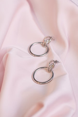 Silver earrings on an expensive pale pink silk background. Beautiful female jewelry. Earrings rings.