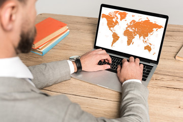 Fototapeta na wymiar cropped view of businessman using laptop with world map on screen isolated on grey