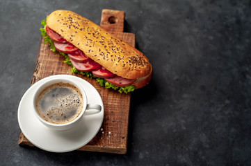 coffee and a large panini sandwich with sausage and cheese in a white plate on a stone background with copy space for your text