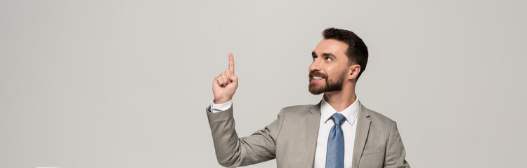 panoramic shot of smiling businessman showing idea gesture isolated on grey