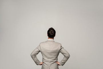 Fototapeta na wymiar back view of businessman standing with hands on hips isolated on grey