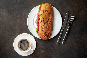coffee and a large panini sandwich with sausage and cheese in a white plate on a stone background with copy space for your text