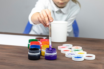 retro style wooden background. It has paint in cans and a brush for painting. A child in a white T-shirt dips a brush in the paint. Close-up. Tinted