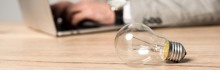 cropped view of businessman using laptop at workplace near light bulb isolated on grey, panoramic shot