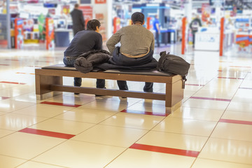 holiday shopping men with women concept. two unrecognizable tired men are sitting on a bench in a...
