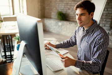 Young entrepreneur working on computer while examining business reports.
