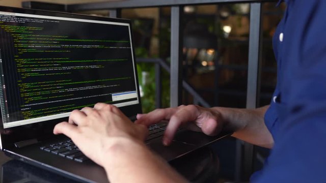 Back view over the shoulder shot of developer programmer with laptop. Program code and script data on the screen. Young freelancer in glasses working on project in cafe.