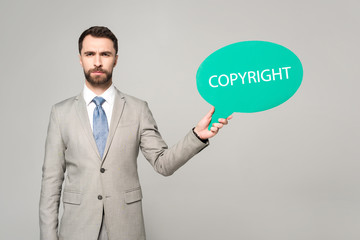 confident businessman holding thought bubble with copyright inscription isolated on grey