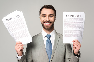 happy businessman holding contracts and looking at camera isolated on grey