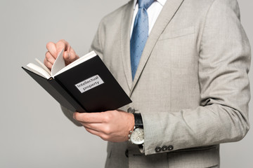 cropped view of businessman reading book with intellectual property title isolated on grey