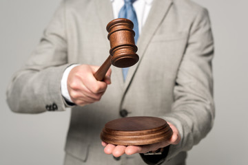 partial view of judge holding gavel isolated on grey