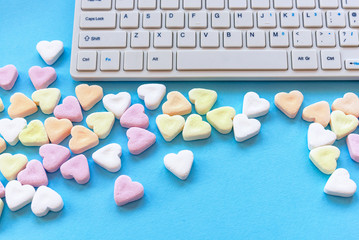 Heart shaped candies and keyboard computer on a blue table. Valentine's day concept. Top view.