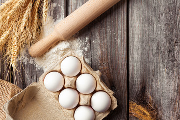 Eggs, flour, wheat ears and rolling-pin on wooden background. Dough ingredients. Top view