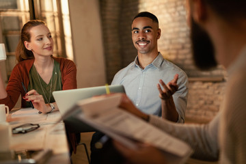 Happy black businessman talking to his coworkers on a meeting in the office.