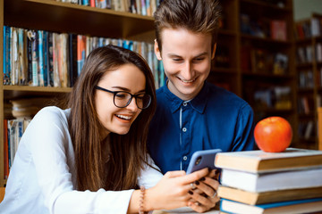 Group of young people sitting in the library. Cheerful students found working with modern devices more convenient and easy then with conventional means