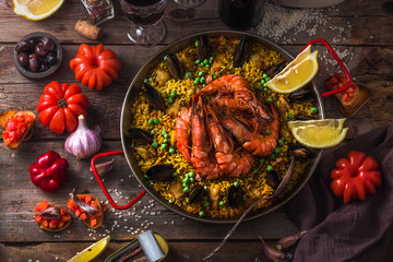 Top view of paella with prawns, mussels and lemon, wooden background