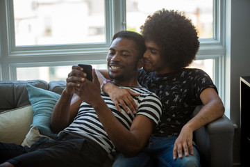 Loving boyfriends looking at smart phone while sitting on sofa at home