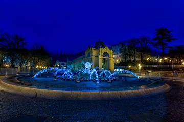 Main cast iron Colonnade and illuminated Singing Fountain (atribut of the city) under snow – winter evening in small Czech spa town Marianske Lazne (Marienbad) – Czech Republic, Europe